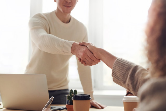 a man behind a desk and laptop shaking hands with a woman